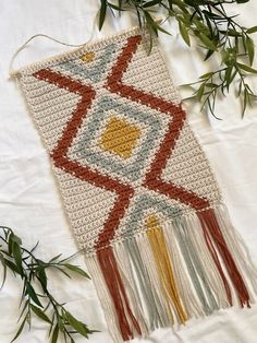 a crocheted wall hanging with green leaves on the side and white fabric behind it