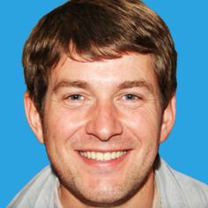 a close up of a person wearing a gray shirt and smiling at the camera with a blue background