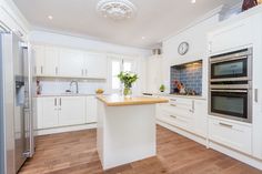 a large kitchen with white cabinets and wood flooring on the counter top, along with an island in the middle