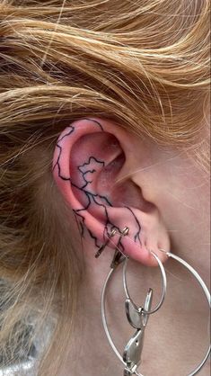 a woman with tattoos on her ear and behind the ear is a pair of hoop earrings