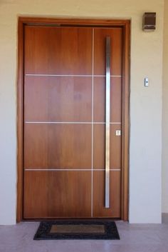 a wooden door in front of a white wall with a black mat on the floor