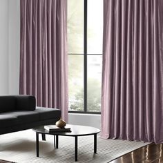 a living room with a couch, coffee table and purple drapes on the window