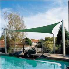 an outdoor swimming pool with rocks and a blue shade sail over it's edge