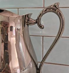 a shiny silver pitcher sitting on top of a counter next to a blue tile wall