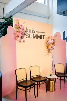 three chairs and a table in front of a pink wall with flowers on it at an exhibition