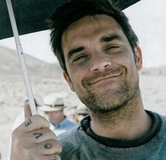 a man holding an umbrella in front of him and smiling at the camera with other people behind him