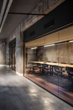 an empty conference room with glass walls and wooden tables in the foreground, along with concrete flooring