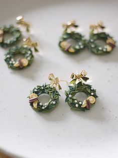 four pairs of christmas wreath earrings sitting on a white plate next to other holiday decorations