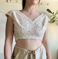 Gorgeous cream lace cropped top with intricate beading in pale pink with some colored rhinestones and sequins scattered throughout.  Unbranded, no label, may even be handmade/ one of a kind.  I'm unsure of the era, I'm guessing that it's 60s or older.  Fits like a modern women's small. Modeled in first two photos on a size small with 28" waist and 35.5" bust without clipping.  Two darts on the front and one in back.  Has 6 snap buttons for the closure on the center back.  Condition overall is excellent. There are no major flaws. No stains, all buttons intact, no missing beading as far as I can tell. There may be some minor snags here and there.  Please refer to measurements for accurate sizing: Shoulders (end to end of sleeve cap) 21" Length: 14" Pit to pit: 19.5" Rib cage: 31" Fitted Party Tops With Intricate Embroidery, Fitted Embellished Beige Blouse, Fitted Lace Beige Crop Top, Fitted Beige Embellished Blouse, Fitted Beige Lace Crop Top, Beige Lace Fitted Crop Top, Feminine Fitted Crop Top For Wedding, Floral Embroidery Cropped Party Top, Intricate Embroidery Fitted Top For Evening