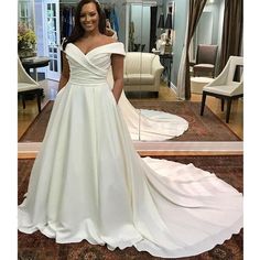 a woman standing in front of a mirror wearing a wedding dress with an off the shoulder neckline