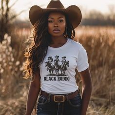 Dive into the essence of Western elegance with our 'Black Rodeo Unisex Tee,' a fashion statement that celebrates heritage and the adventurous spirit of three stunning Black women on their majestic rides. Perfect for individuals passionate about Western equestrian culture, heartland melodies, and the vibrant traditions of rodeo, this tee is a tribute to the enduring strength of cowgirl legends. Crafted from premium soft materials for ultimate comfort and durability, it's ideal for any setting, fr Cattle Barons Ball Outfit, Women Cowboy Outfits, Country Outfit Black Women, Fitted Band Merch Shirt, Band Merch Tops With Custom Print, Country Outfits Black Women, Black Cowgirl Outfits For Women, Cali Cowgirl, Black Rodeo Outfits For Women