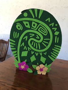 a green paper sculpture sitting on top of a wooden table next to a flower vase