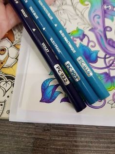 two blue pencils sitting on top of a piece of paper next to an adult coloring book