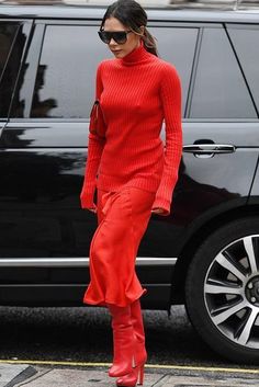 a woman in red is walking down the street with her legs crossed and wearing high heeled boots