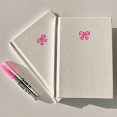 two notebooks with pink bows on them next to a marker and eraser pen