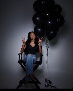 a woman sitting in a chair with black balloons on her head and one hand up