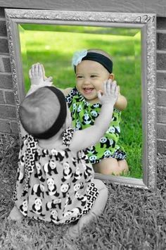 two babies sitting in front of a mirror on the grass, one holding his hands up