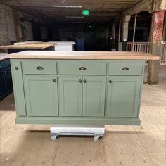 a green kitchen island with wooden top on casteors in an unfinished warehouse flooring area