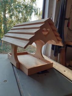 a wooden birdhouse sitting on top of a table next to a window with trees in the background