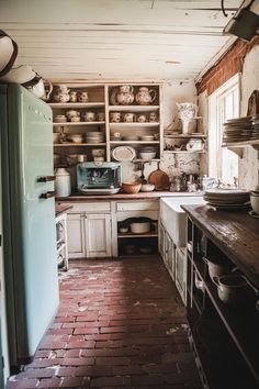 an old fashioned kitchen with brick floors and lots of dishes on the shelves above the stove