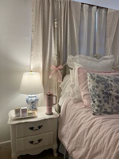 a white bed sitting next to a window covered in pink and blue pillows on top of a wooden dresser