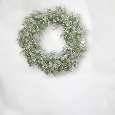 a wreath with white flowers and green leaves on a white background, hanging from the wall