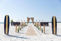 an outdoor ceremony setup on the beach with blue and yellow surfboards in the sand