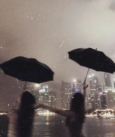 two people holding umbrellas in front of a cityscape at night with rain falling on them