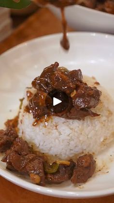 a white plate topped with rice covered in meat and sauce on top of a wooden table