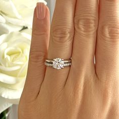 a woman's hand with a diamond ring on it and white roses in the background