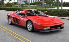 a red sports car is parked on the side of the road in front of some palm trees