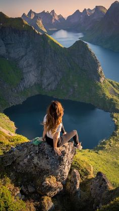 a woman sitting on top of a large rock next to a body of water in the mountains