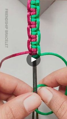 someone is holding the end of a piece of green and pink thread with two hands