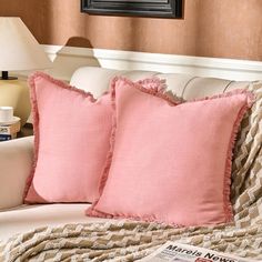 two pink pillows sitting on top of a white couch next to a pillow with ruffled edges