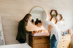 a woman standing next to a baby in a crib and looking at her reflection