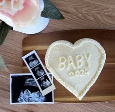 a wooden cutting board topped with a heart shaped cake next to an envelope and photos