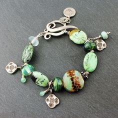 "Beautiful green turquoise oval gemstones are combined with sterling silver, and my lampwork glass beads in this handmade bracelet. Sweet sterling silver charms dangle from the bracelet, as well as my tiny fine silver and glass beads. A decorative sterling silver toggle clasp and a dangle of a lotus flower silver charm complete the design. So perfect for Spring and Summer! This lovely new bracelet will fit an 7\" wrist and can be re-sized at no extra charge. Your bracelet will arrive artfully pa Handmade Green Bracelets With Oval Beads, Green Sterling Silver Beaded Bracelet, Green Sterling Silver Bracelets With Silver Beads, Green Sterling Silver Bracelets With Round Beads, Green Sterling Silver Bracelet With Silver Beads, Spiritual Green Beaded Sterling Silver Bracelets, Unique Green Sterling Silver Bracelets, Lampwork Bracelets, New Bracelet