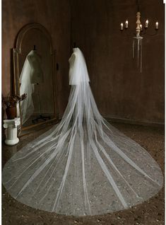 a wedding dress with a long veil on display in front of a mirror and chandelier