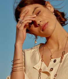 a woman with her hands on her face and wearing rings, necklaces and bracelets