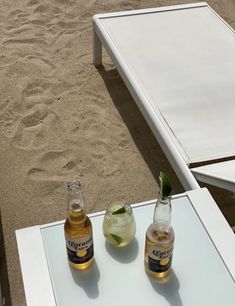 two bottles of beer sitting on top of a glass table next to a beach chair