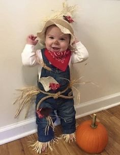 a small child wearing overalls and a cowboy hat standing next to a pumpkin on the floor