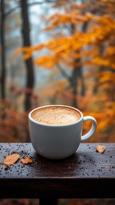 a cup of cappuccino sitting on top of a wooden table in front of trees