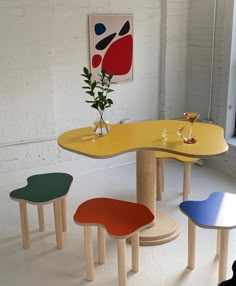 four different colored tables and chairs in a room with white walls, one has a vase on the table