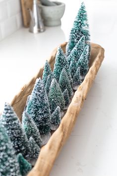 small christmas trees in a wooden tray on a counter top, with snow falling off the tops