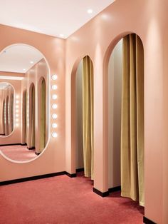 a pink room with mirrors and lights on the walls, along with curtains in front of them