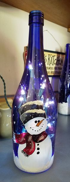 a glass bottle with a snowman painted on the side and lights in the top