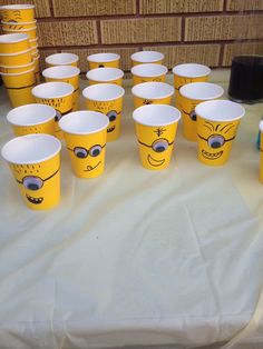 yellow cups with faces drawn on them sitting on a white tablecloth covered table cloth