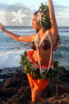 a woman in an orange and white hula dancing on the rocks by the ocean