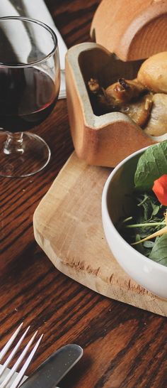 a wooden table topped with a white bowl filled with food and a glass of wine