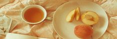 an apple and two pieces of fruit on a plate next to a cup of tea